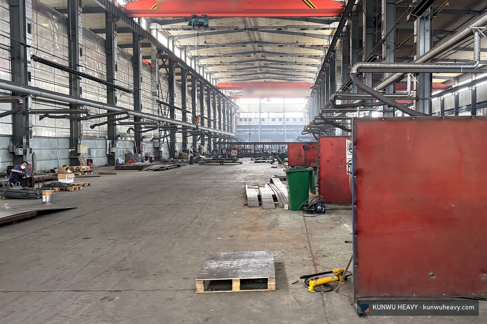 Welding bays behind red screens in the fabrication hall, welder at work